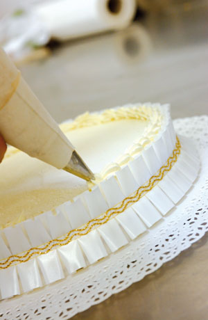 Decorazione torta con sac à poche. Panna montata, bordo dorato e merletto. Pasticceria artigianale.