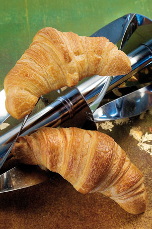 Due croissant dorati su supporto in metallo. Colazione italiana, pasticceria, panetteria.