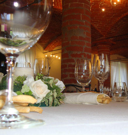 Tavolo elegante ristorante: calici, fiori bianchi, grissini e pilastro in mattoni. Cena romantica.