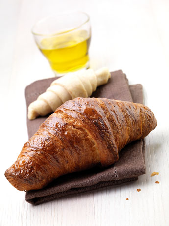 Croissant dorato su tovagliolo con bicchiere di succo. Pasticceria e colazione.