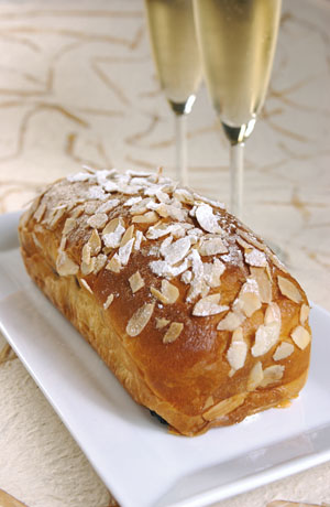 Brioche alle mandorle su piatto bianco con flute di spumante. Dolce da forno artigianale.