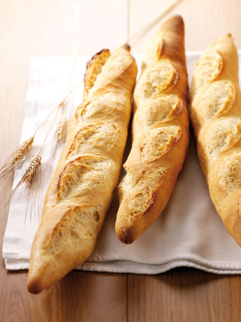 Tre baguette dorate su un panno bianco con spighe di grano. Pane fresco, croccante.