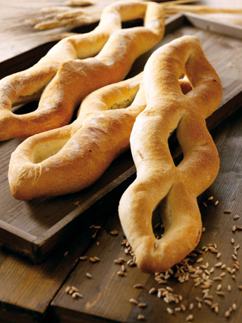Pane artigianale a forma di ferro di cavallo su vassoio di legno. Grano sparso. Panetteria italiana.
