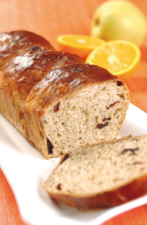 Pane dolce con uvetta, fetta tagliata. Arance e mela sullo sfondo. Ricetta tradizionale, colazione gustosa.