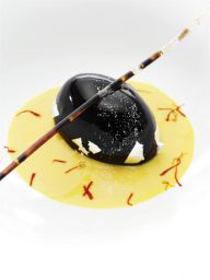 Dessert gourmet: sfera nera lucida con salsa gialla e decorazioni. Cucina creativa.