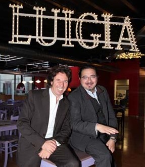 Pizzeria Luigia: due uomini sorridenti sotto l'insegna luminosa LUIGIA. Ristorante italiano, atmosfera accogliente.