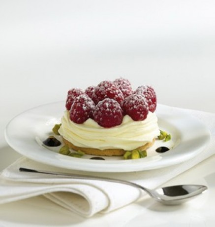 Dolce con mousse, lamponi freschi e pistacchi. Dessert elegante su piatto bianco.