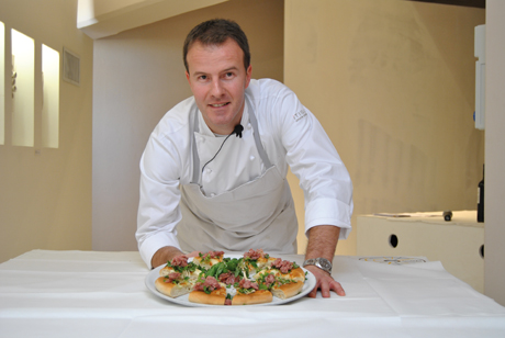 Chef con pizza gourmet. Ritratto di cuoco italiano con piatto di pizza artigianale. Cucina italiana.