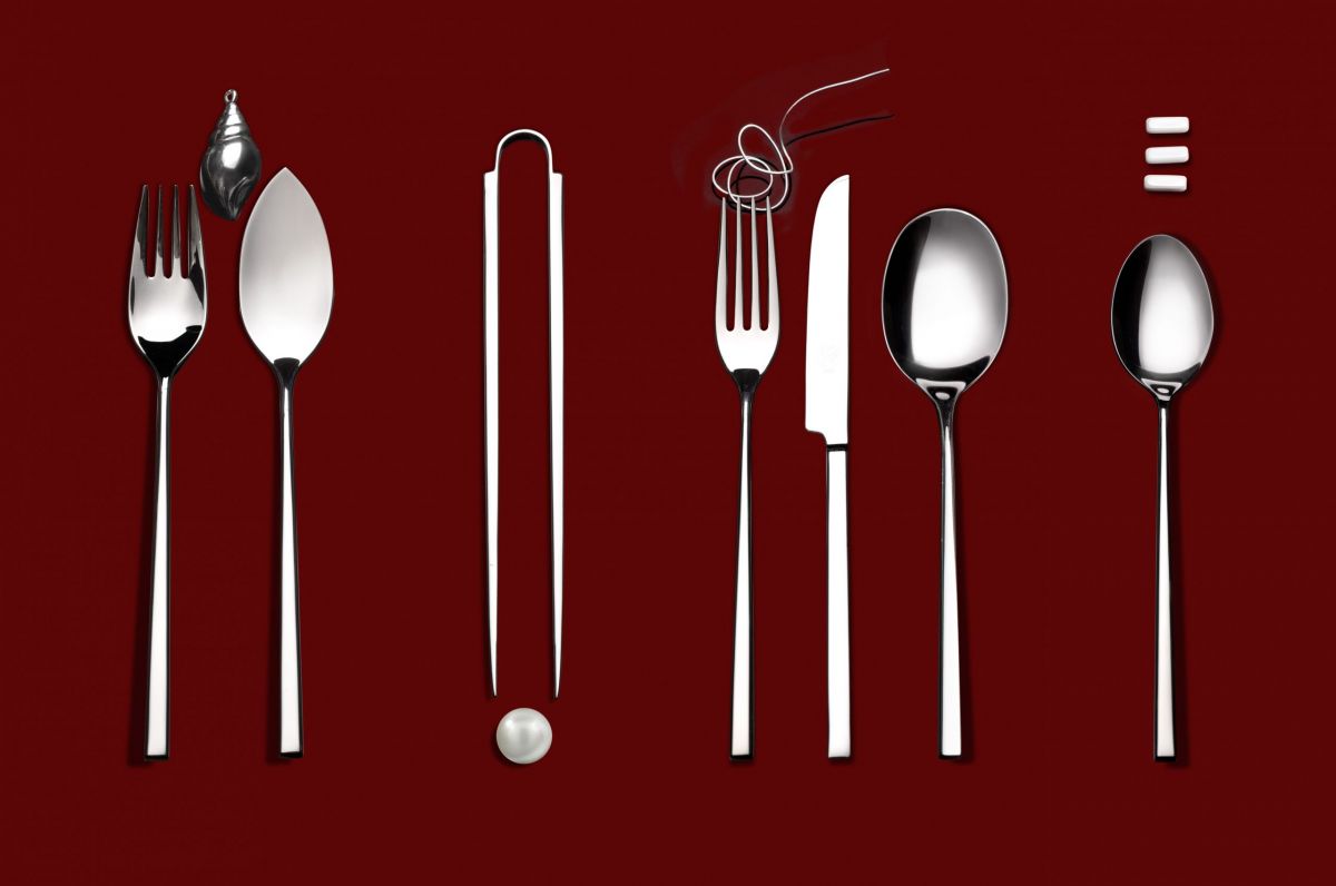 Set di posate Marchesi su sfondo bordeaux. Design moderno con forchetta, coltello, cucchiaio e accessori tavola.