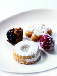 Dolci assortiti su piatto: tortino, more, lamponi e frittelle zuccherate. Delizie dolci per ogni gusto.