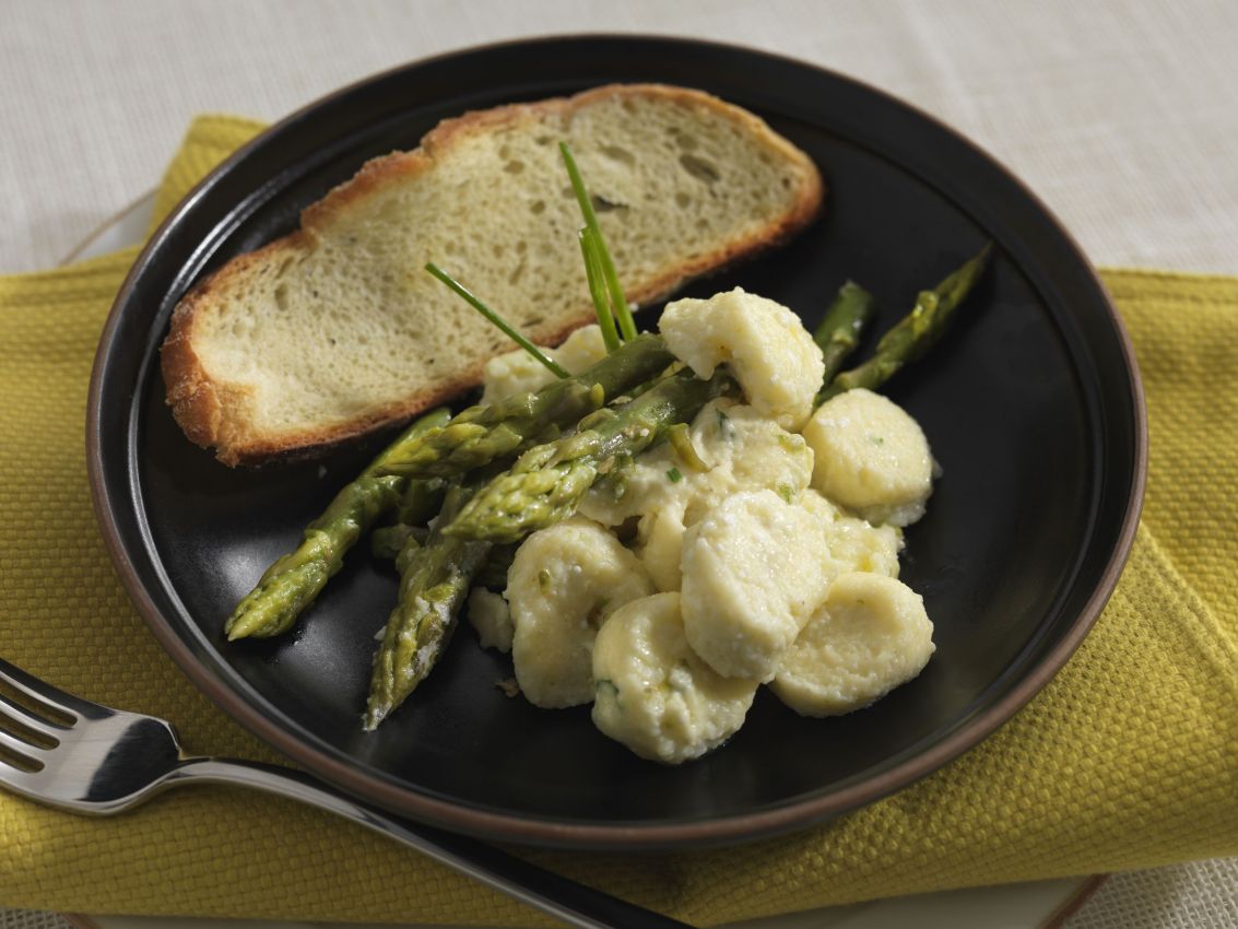 Gnocchi di Sbrinz e ricotta con asparagi e pane su piatto nero. Ricetta primaverile.