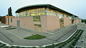 Architettura moderna: edificio con facciata in vetro e parcheggio. Design urbano, illuminazione interna.