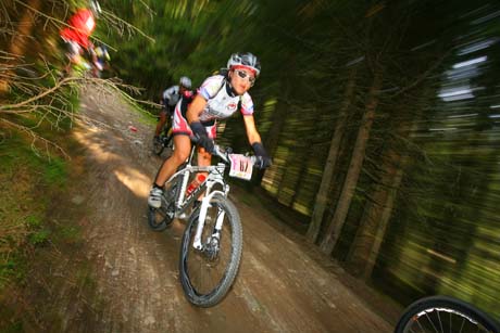 Donna in mountain bike durante gara di cross-country. Percorso sterrato nel bosco. Sport e natura.