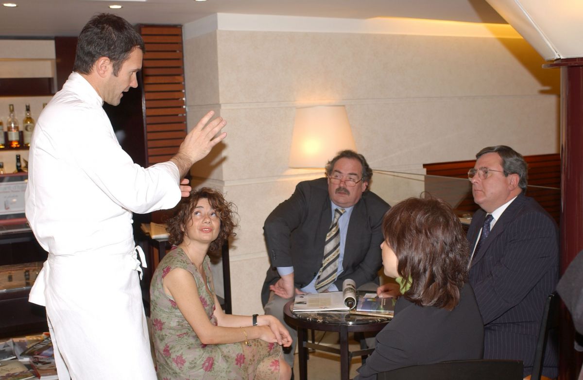 Lo chef Cracco parla a un gruppo di persone sedute a un tavolo. Ristorante, cucina italiana.