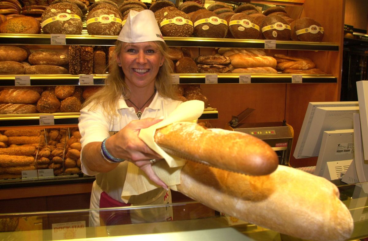 Panificio artigianale: donna sorridente offre pane fresco. Scaffali pieni di pane e prodotti da forno.