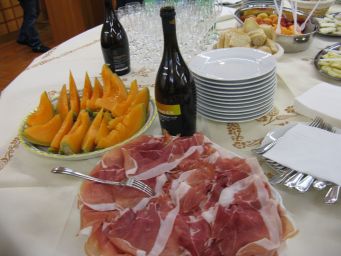 Buffet italiano: melone, prosciutto, bottiglie di vino, piatti e posate. Catering per eventi e feste.