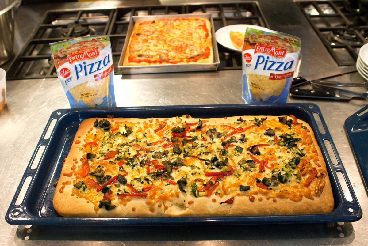 Pizza fatta in casa con formaggio Entremont, verdure fresche. Pizza rettangolare in teglia blu.