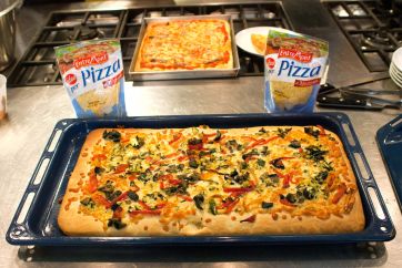 Pizza fatta in casa con formaggio Entremont, verdure fresche. Pizza rettangolare in teglia blu.