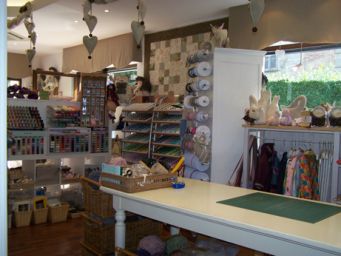 Interno negozio di cucito: bancone bianco, scaffali con fili colorati, tessuti e accessori per hobby creativi.