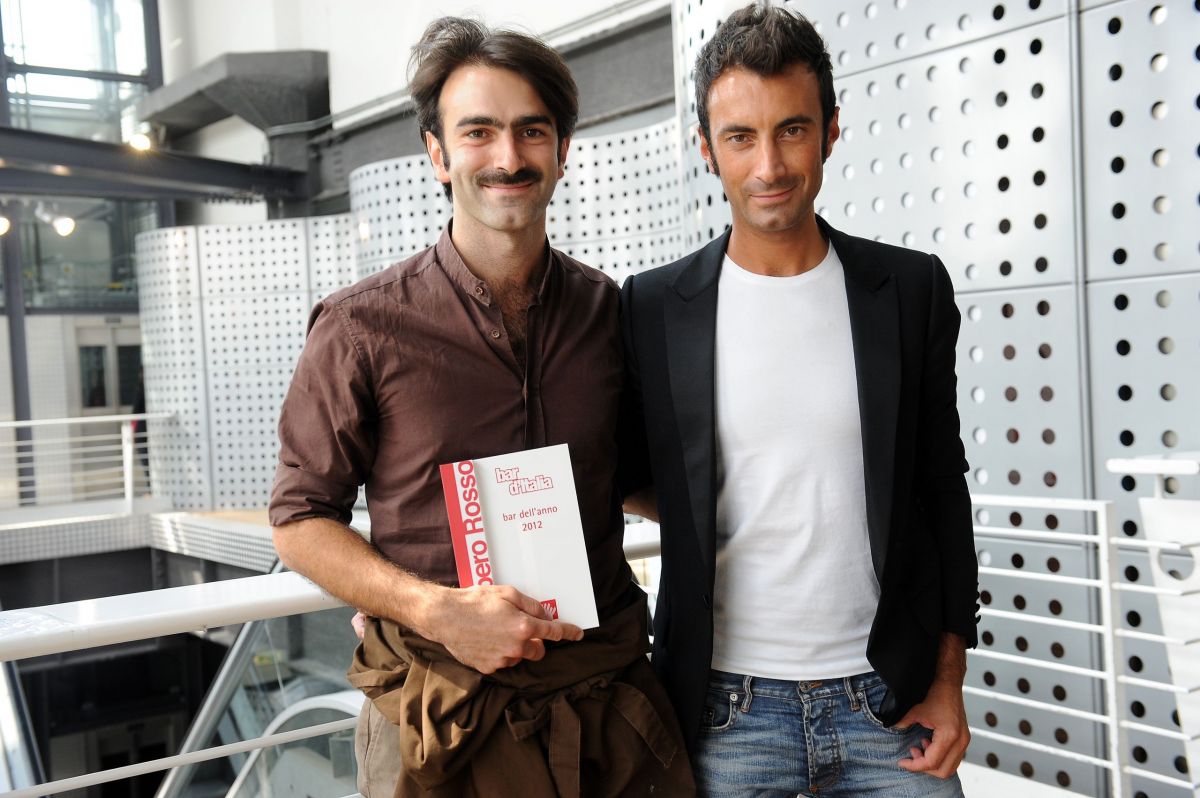 Due uomini sorridenti con libro Gambero Rosso. Moda uomo, stile italiano.