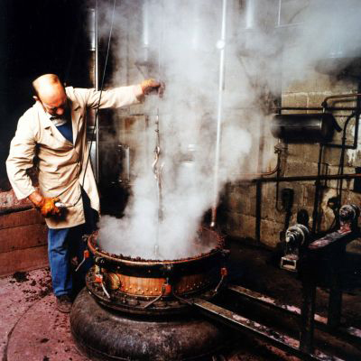 Mastro distillatore al lavoro. Alambicco in rame con vapore. Produzione artigianale di grappa.