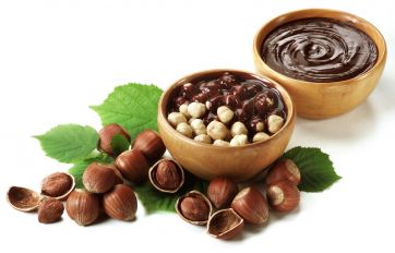 Nocciole e crema al cioccolato. Ciotole di legno con nocciole sgusciate e cioccolato fuso.