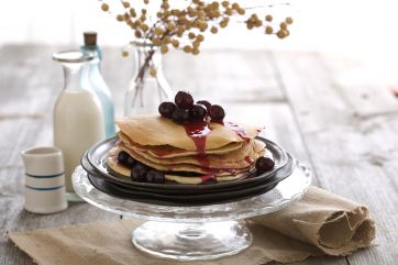 Pancake all'amarena su alzata di vetro. Colazione dolce con frutti di bosco e sciroppo. Ricetta pancake.