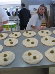 Donna prepara focaccia pugliese con olive. Cucina tradizionale italiana, prodotti da forno freschi.