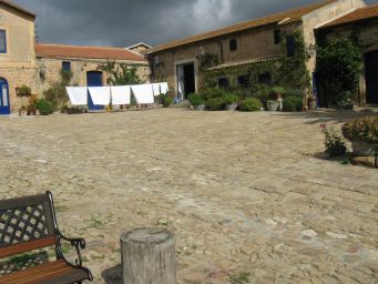 Cortile in pietra di masseria siciliana con panni stesi, panchina e cielo nuvoloso. Architettura rurale, Sicilia.