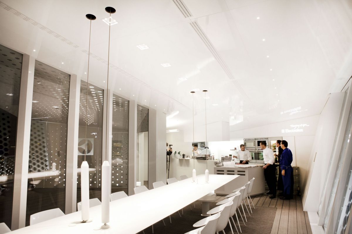 Interno di Electrolux The Cube a Milano. Design minimal, tavolo lungo bianco, chef in cucina.