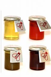 Quattro vasetti di miele artigianale di diversi colori con etichetta ape.