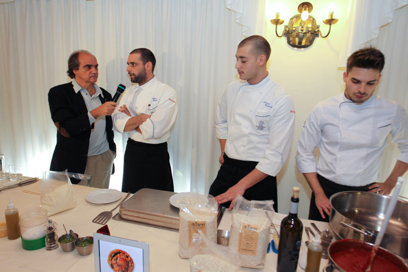 Chef intervistato durante evento culinario. Tavolo con ingredienti e utensili da cucina.