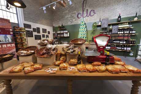 Gastronomia italiana: tavolo con pane, cesti di salumi, bilancia rossa vintage e scaffali di vino. Prodotti tipici.