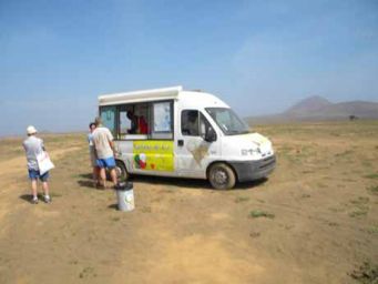 Furgone gelati nel deserto. Persone comprano gelato. Paesaggio arido con cielo azzurro. Vacanze, estate.