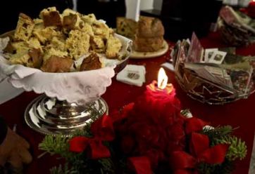 Centrotavola natalizio con panettone artigianale a pezzi, candela rossa e decorazioni festive.