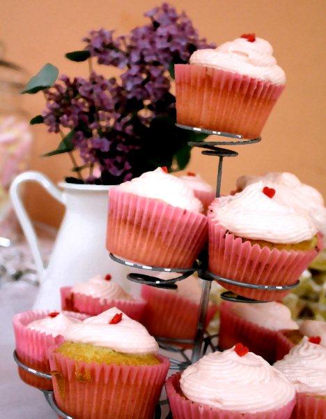 Cupcakes rosa con cuori su alzatina. Fiori lilla, dolci da forno, dessert, pasticceria.