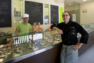 Gelateria artigianale italiana: gelatai sorridenti dietro il bancone con gusti gelato scritti sulla lavagna.