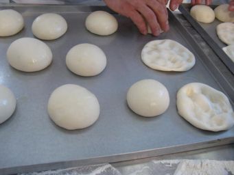 Preparazione pizza napoletana: palline di pasta lievitata su teglia. Mani che stendono l'impasto.