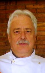 Ritratto di Pino Scaringella, chef italiano con divisa bianca e baffi. Cucina italiana.