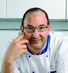 Ritratto di chef italiano Montanari con divisa bianca e dettagli tricolore. Cucina italiana, alta gastronomia.