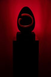 Scultura moderna: uovo nero con cerchio rosso su piedistallo. Arte contemporanea, design minimalista.