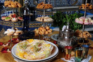 Dolci marocchini assortiti su vassoi d'argento. Torta con frutta fresca, teiera e bicchieri decorati. Cucina tradizionale.