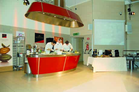 Cucina professionale Academia Barilla: chef al lavoro. Design moderno, illuminazione scenica. Corsi di cucina e show cooking.