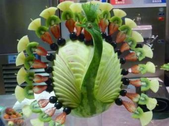 Scultura di frutta a forma di pavone. Decorazione creativa con melone, kiwi, fragole e mirtilli. Idea per buffet e feste.