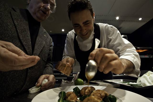 Chef cucina piatto gourmet. Preparazione professionale con salse e guarnizioni. Esperienza culinaria di alta qualità.