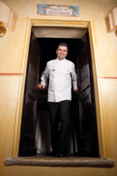 Ritratto chef ristorante italiano. Sorridente, in divisa bianca, accogliente. Cucina tipica.