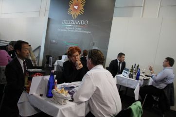 Vinitaly: Degustazione vini Deliziando Emilia-Romagna. Persone a tavola durante evento enogastronomico. Fiera del vino.