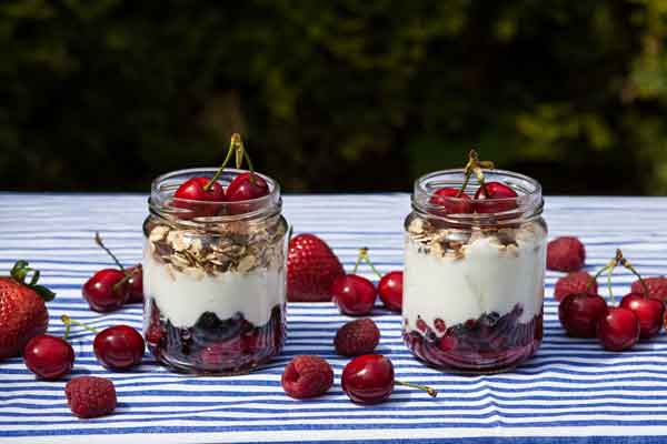 Dolci in barattolo con yogurt, granola e frutti di bosco freschi. Dessert estivo sano e gustoso.
