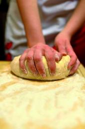 Impasto fatto in casa. Mani che lavorano la pasta su un tavolo infarinato. Ricetta, cucina, panificazione.