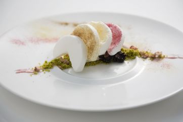 Dolce gourmet su piatto bianco. Meringhe colorate, frutti di bosco e granella. Alta cucina, dessert creativo.